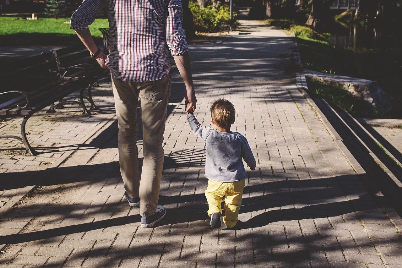 Photo of a father leading a small child shown from the back