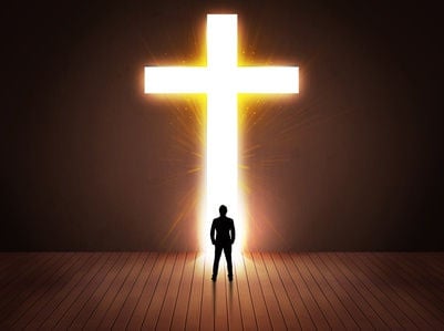 Photo of a man standing in front of a large back lit cross