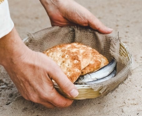 Photo of hands holding a small basket containing bread and small fish