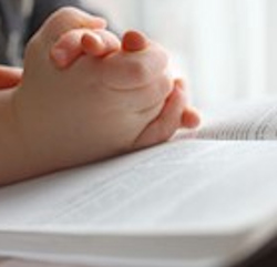 child's folded hands on open bible