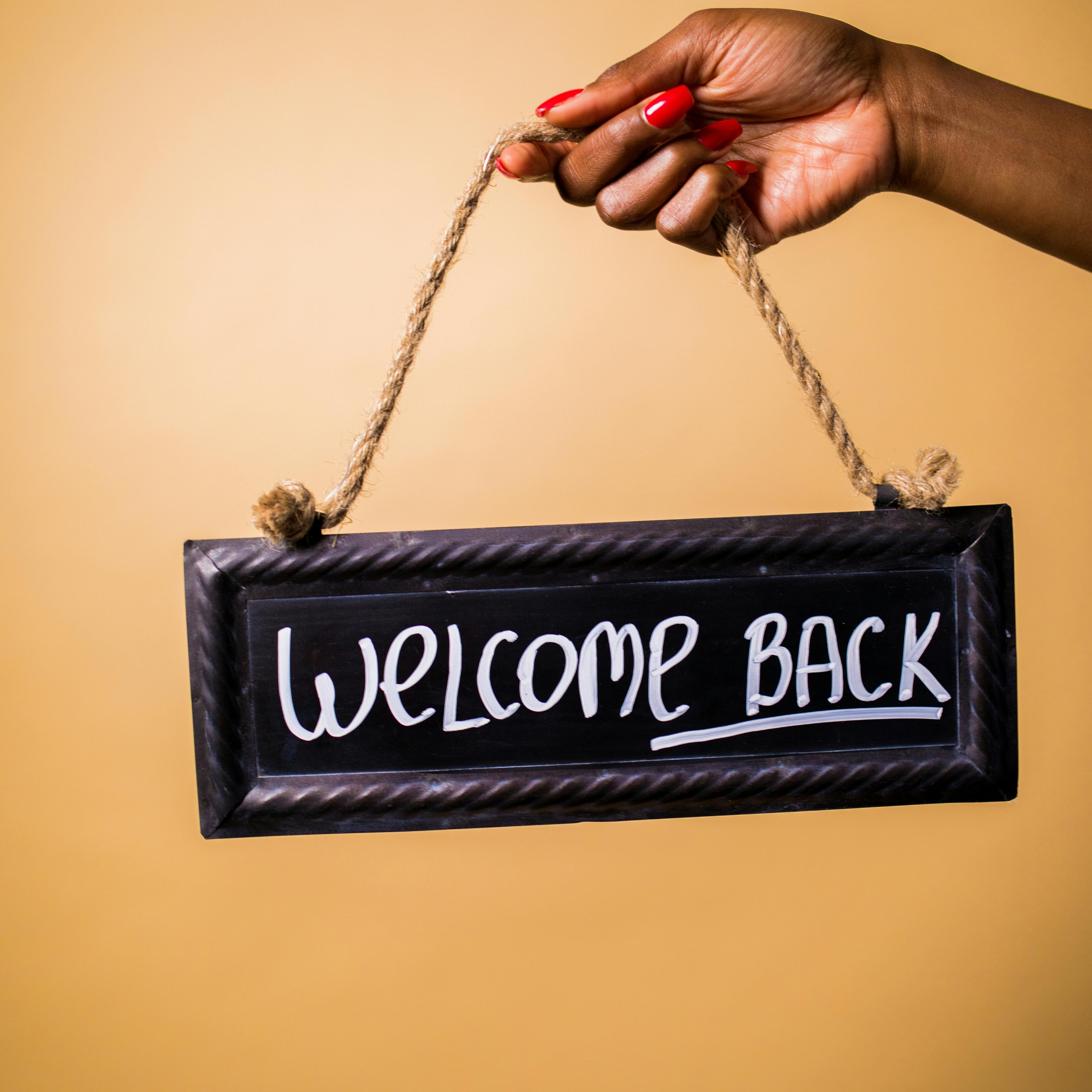 Photo of a hand holding a sign that reads Welcome Back